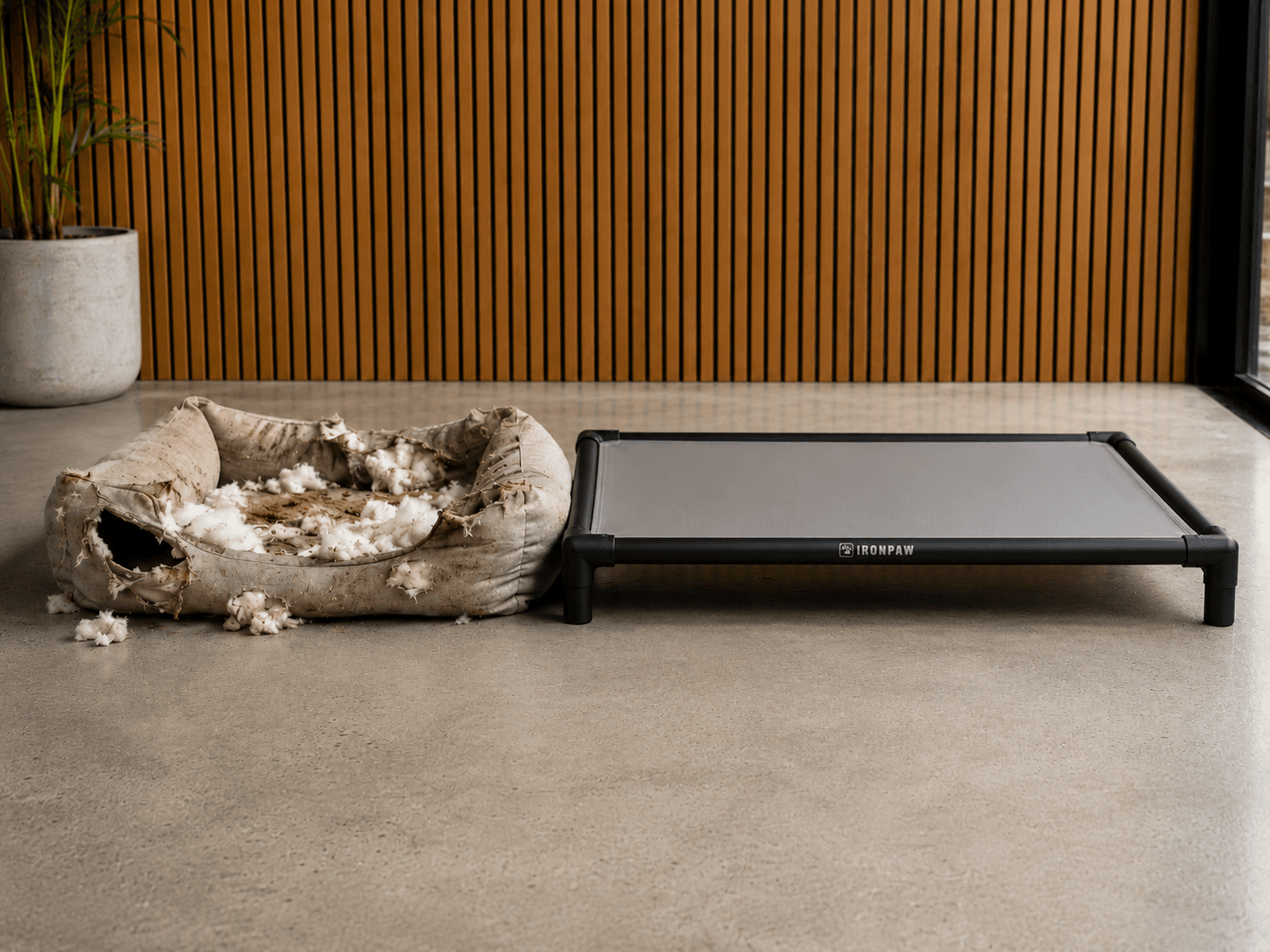 Side-by-side flat lay comparison showing a shredded foam dog bed with stuffing pulled out on the left and a clean elevated aluminium frame dog bed with enclosed dark PVC fabric and no exposed fabric edges on the right, photographed on a neutral background.